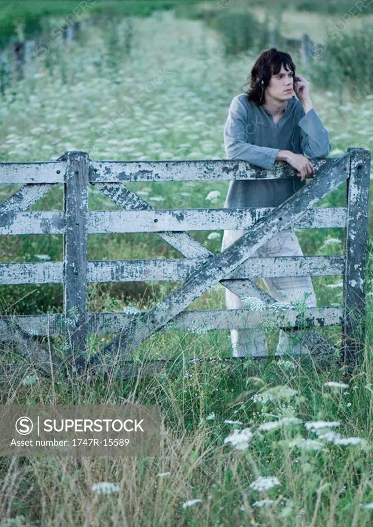Man leaning on wooden fence, listening to headphones