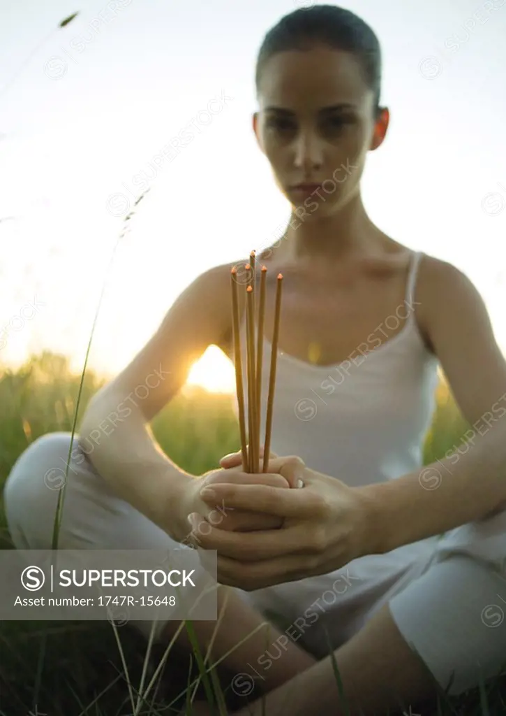 Woman holding sticks of burning incense while sun sets
