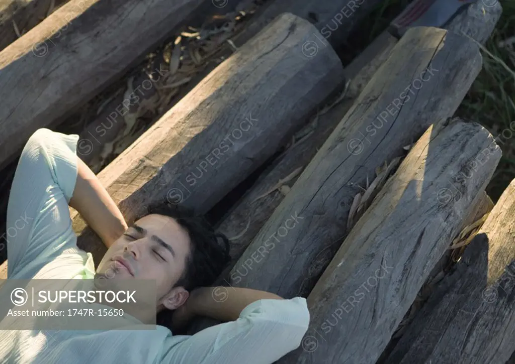 Man lying on logs, eyes closed