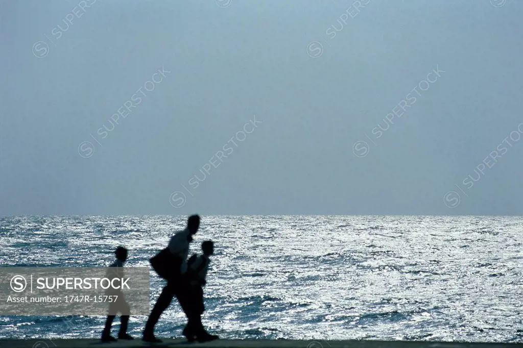 Man walking with two sons, silhouetted against ocean
