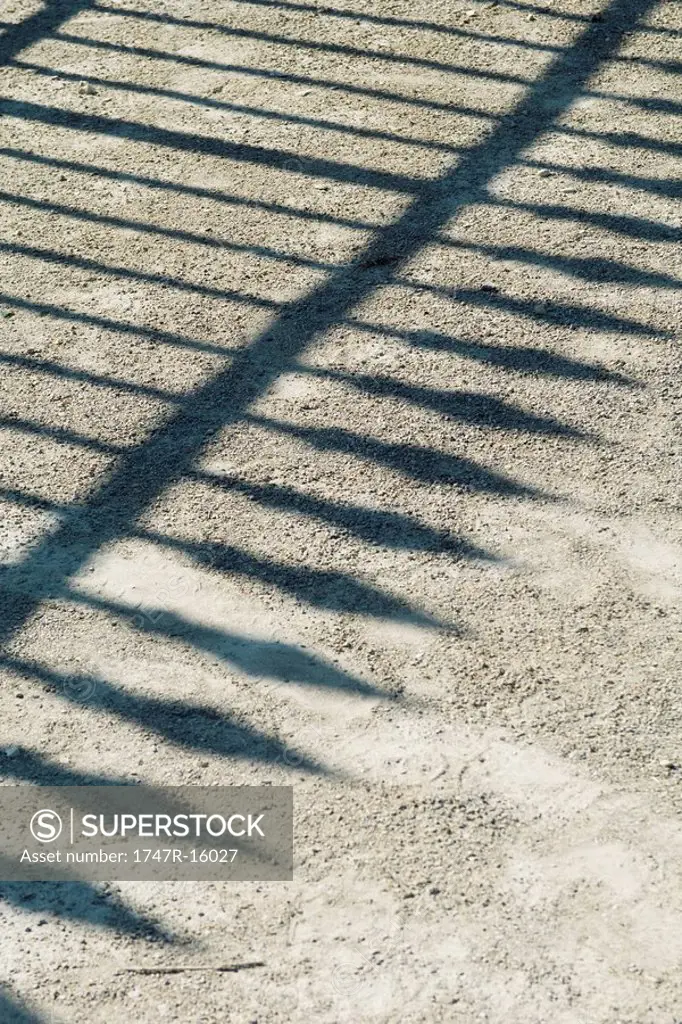 Shadow of wrought iron fence on gravel