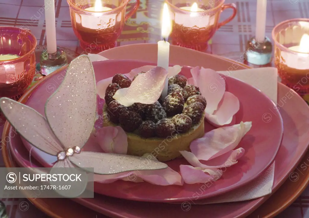 Raspberry pastry on plate decorated with rose petals and candles