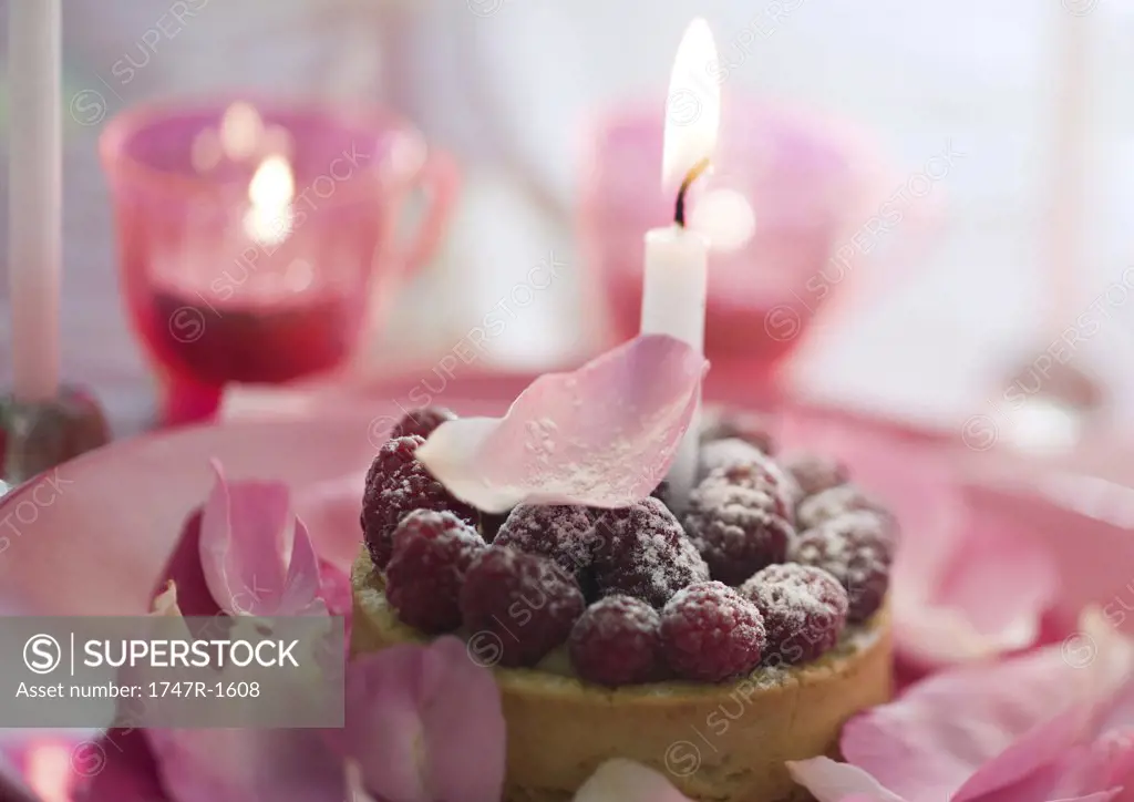 Raspberry pastry on plate decorated with rose petals and candles