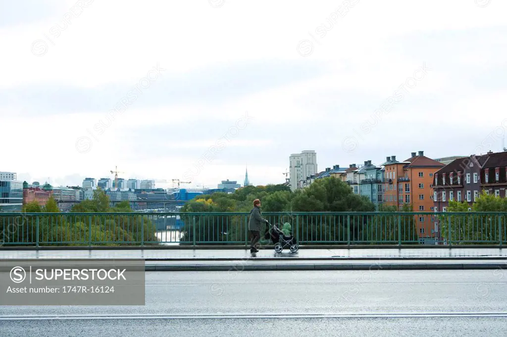 Sweden, Stockholm, woman pushing baby stroller across bridge