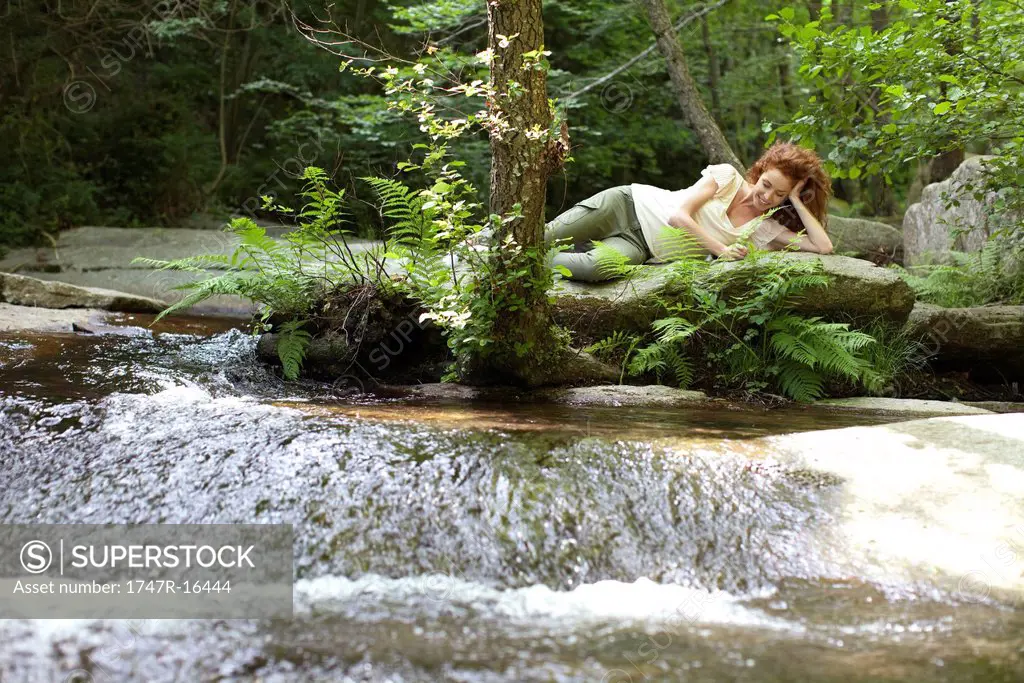 Young woman relaxing on rock by flowing stream