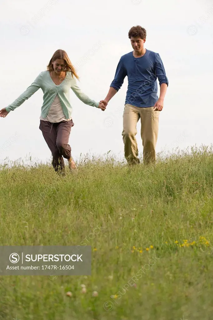 Young couple walking on meadow holding hands