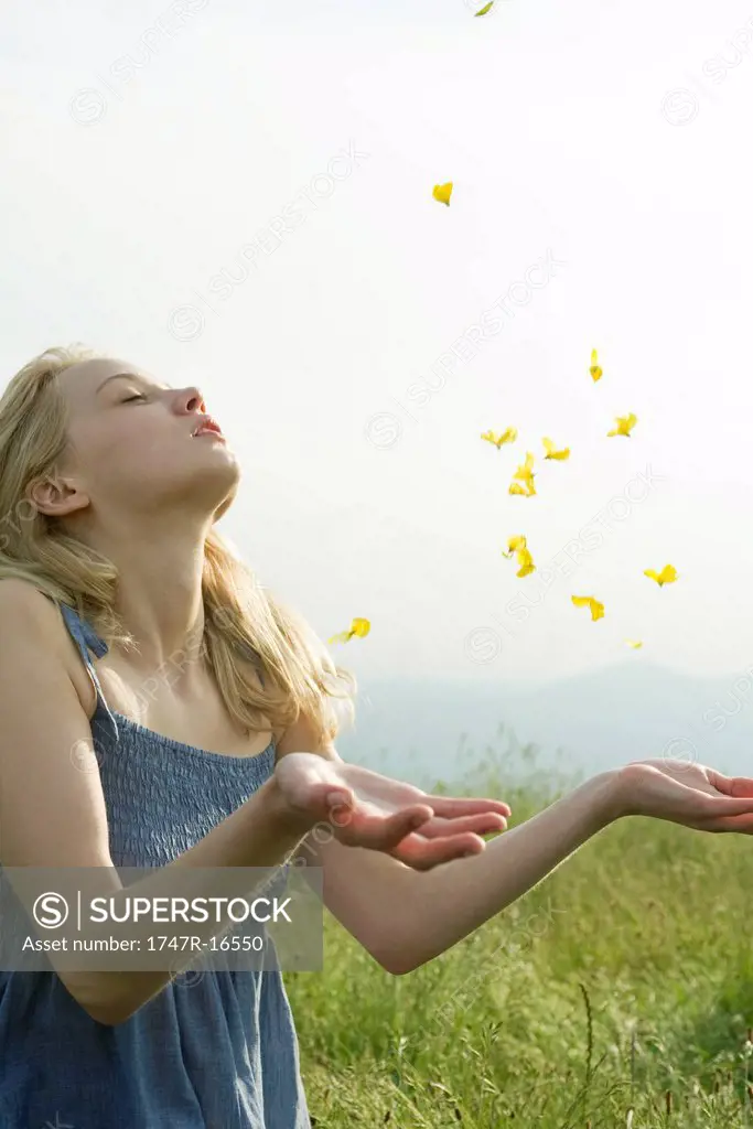 Young woman in field, with eyes closed, throwing flower petals in air