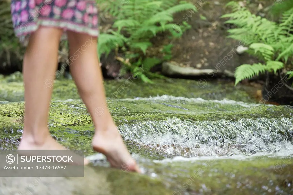 Young woman dipping toes in stream, cropped