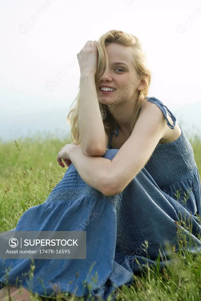 Young woman sitting in field of grass, portrait