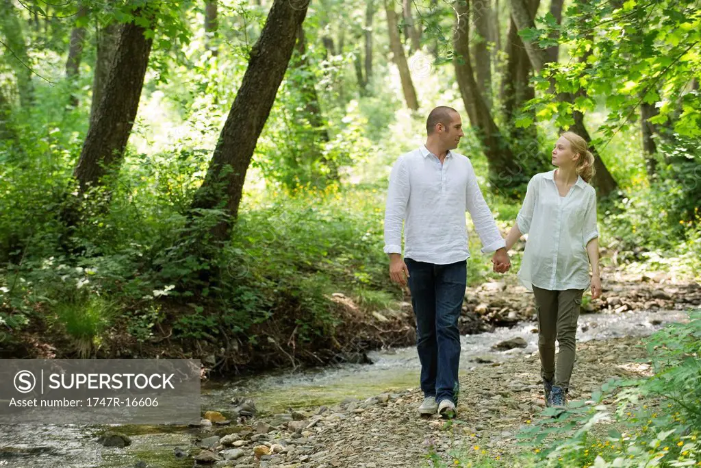 Couple walking by stream running through woods
