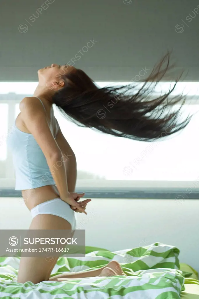Young woman kneeling on bed tossing hair
