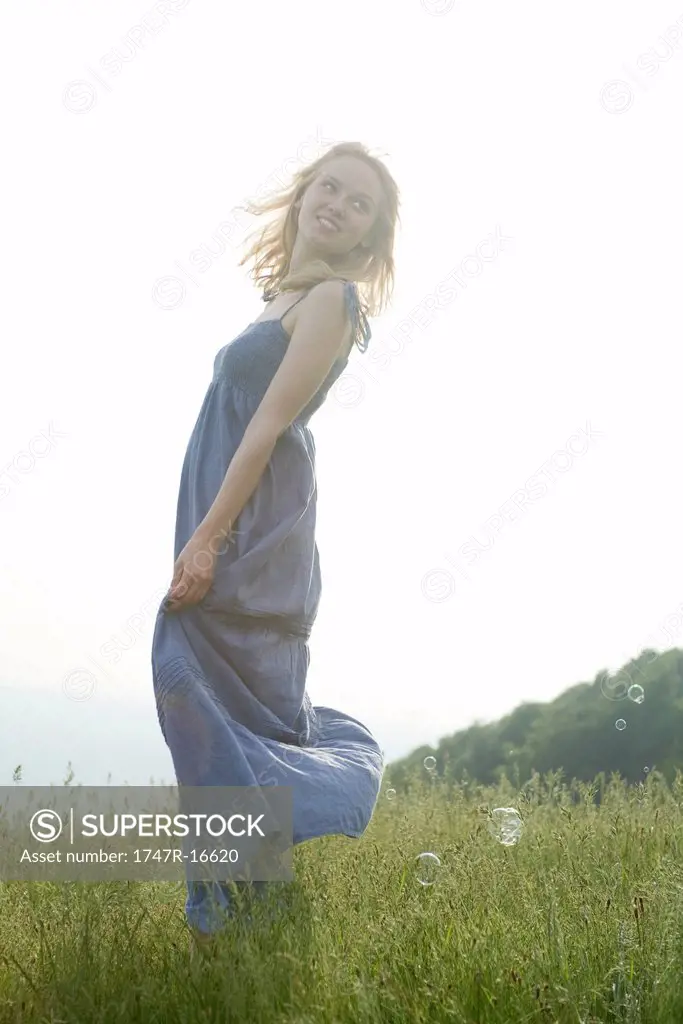Young woman standing in meadow on breezy day, bubbles floating around her