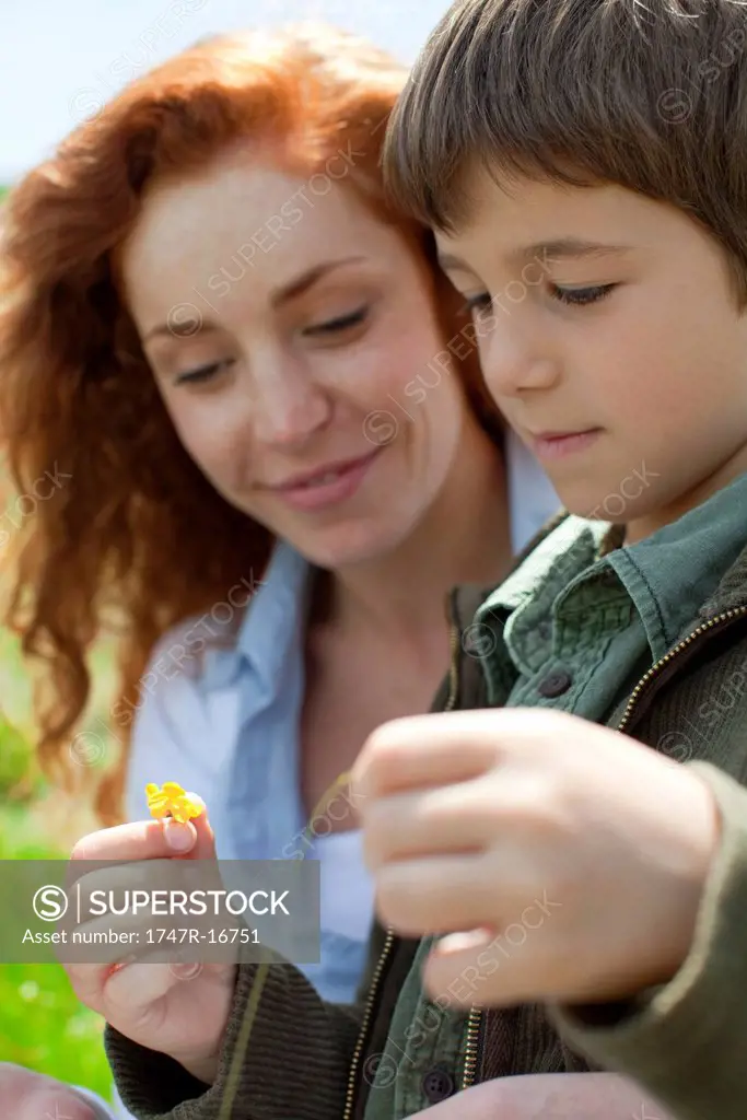 Boy looking at flower outdoors with his mother
