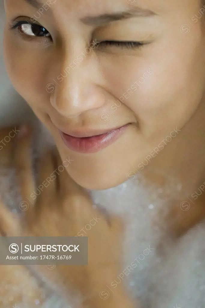 Young woman taking bubble bath, winking, high angle view