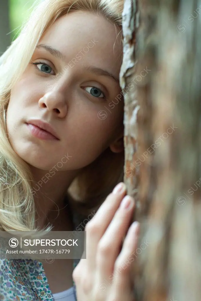 Young woman leaning against tree, portrait