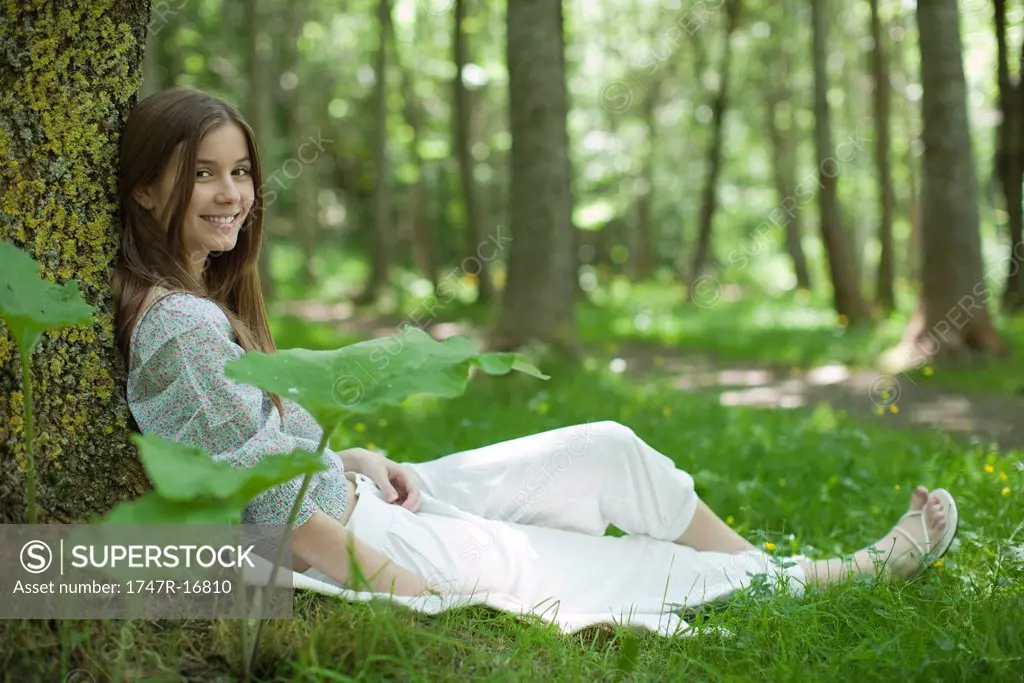 Young woman sitting against tree in woods, portrait