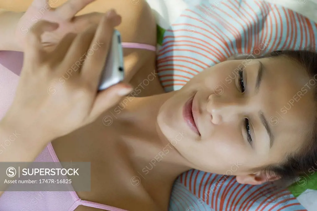 Young woman lying on bed text messaging