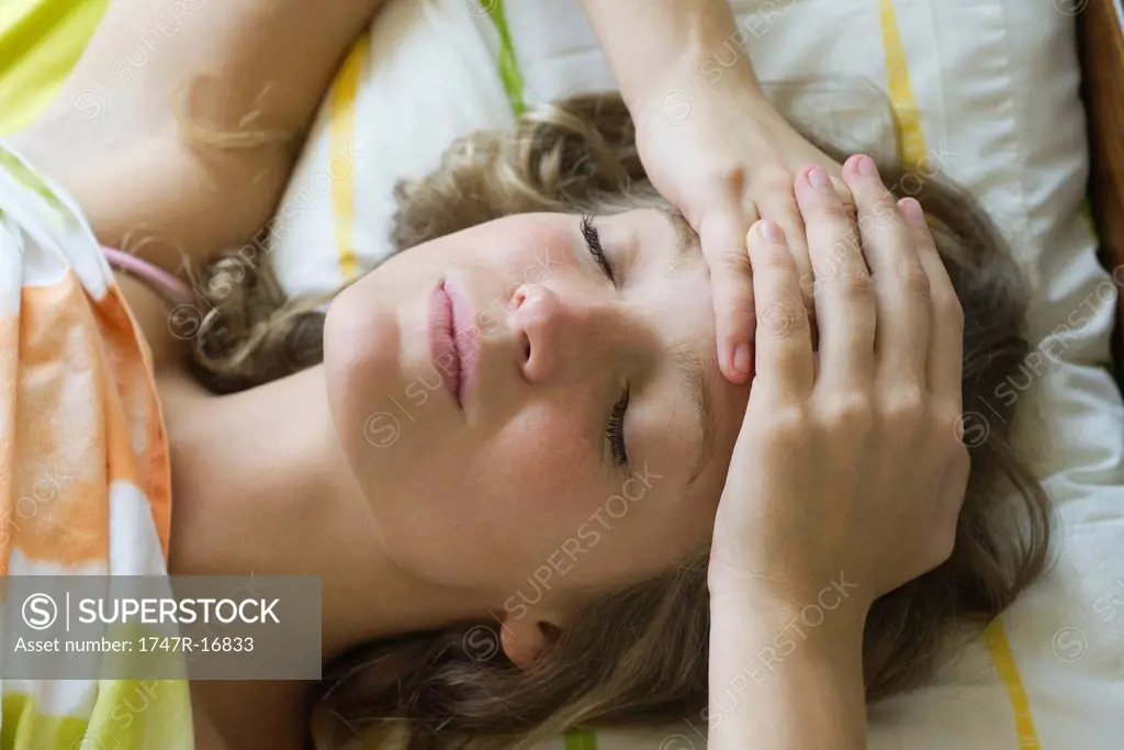 Young woman lying in bed with hands clasped on forehead