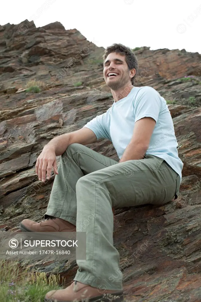 Man laughing while sitting on rock, low angle view