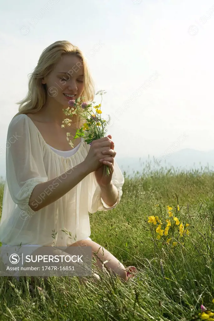 Young woman kneeling in meadow, smelling bouquet of wildflowers
