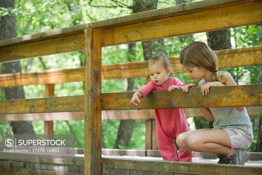 Baby girl and older sister looking over railing of bridge