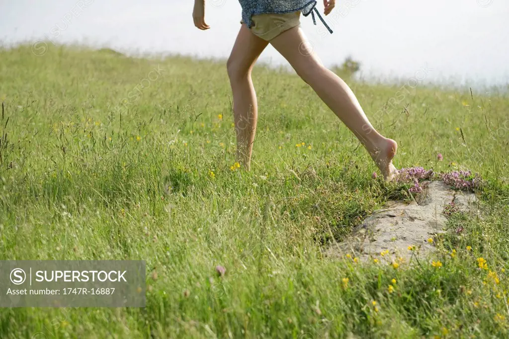 Woman running on meadow with bare feet, low section