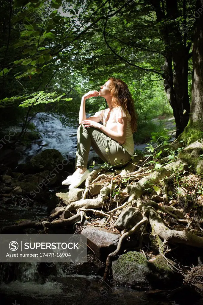 Young woman sitting by stream in woods