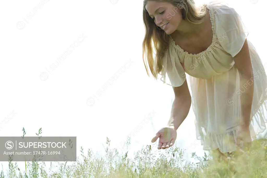 Young woman bending over to touch tall grass