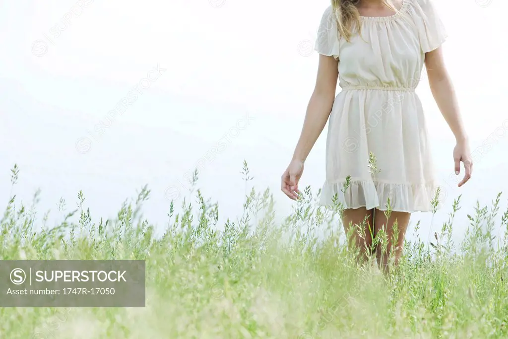 Young woman walking in tall grass, cropped