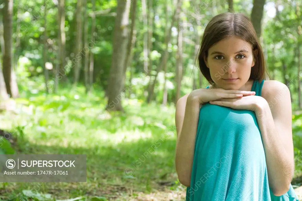 Young woman sitting in woods with chin resting on knees, portrait