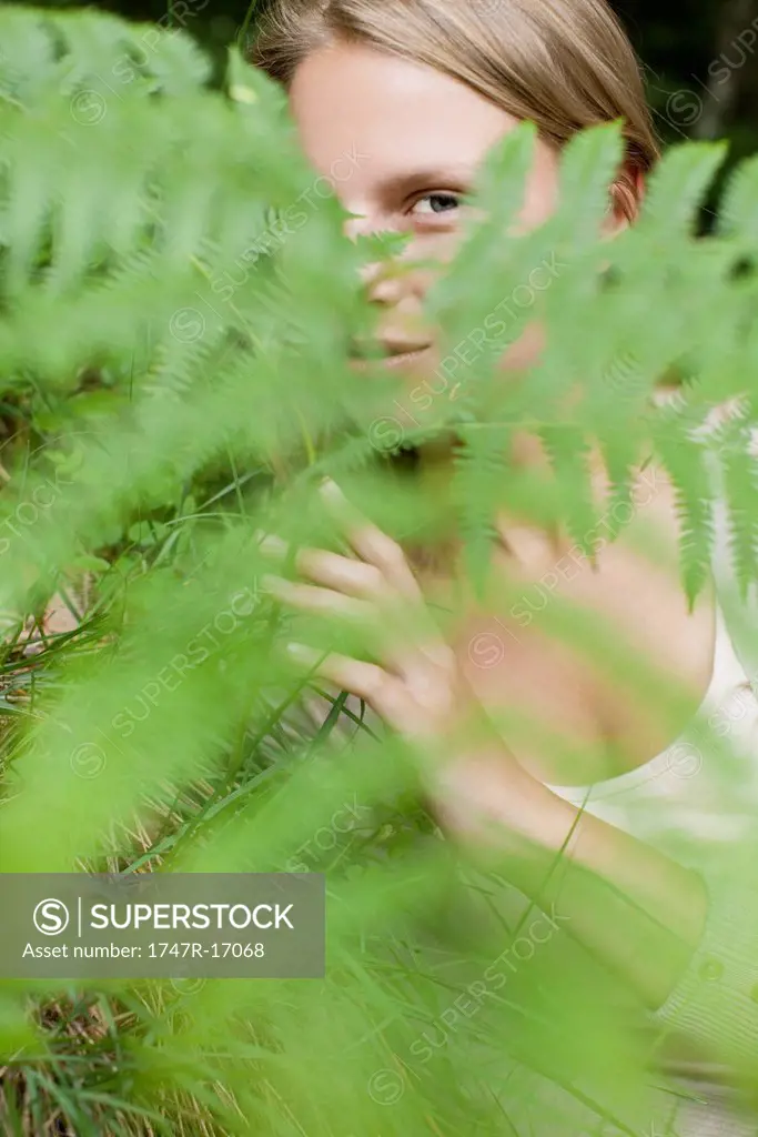 Woman peeking through fern frond, portrait