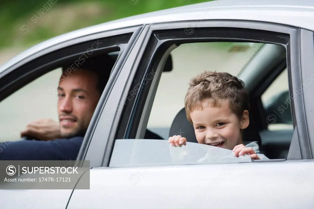 Father and son smiling out car window at camera