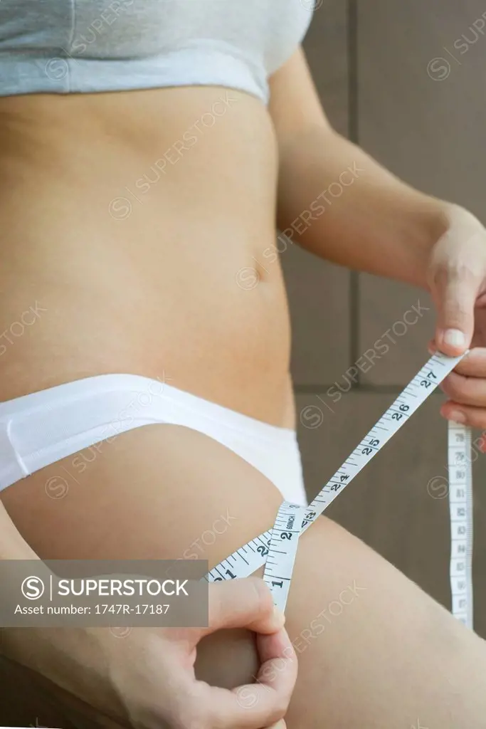 Young woman measuring thigh with measuring tape, cropped