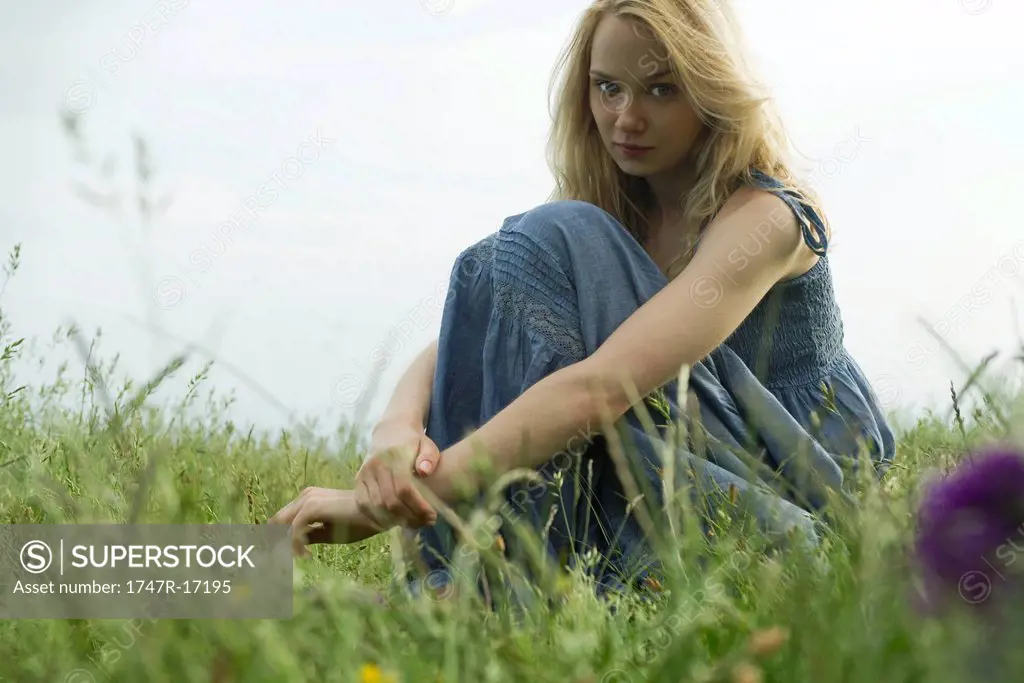 Young woman sitting in field of grass, portrait