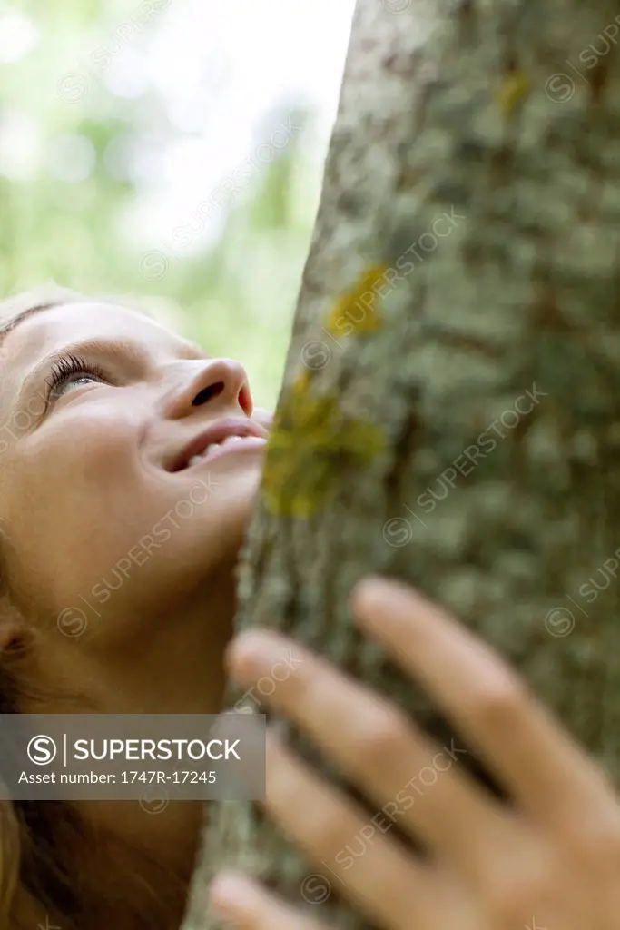 Young woman hugging tree, cropped