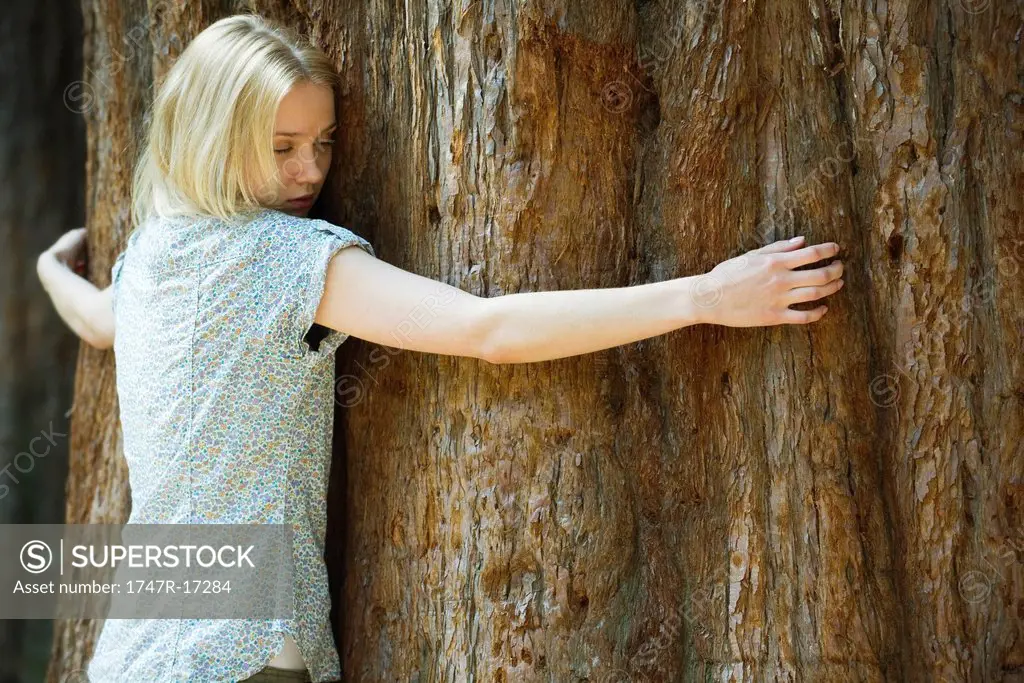 Young woman hugging tree trunk with eyes closed