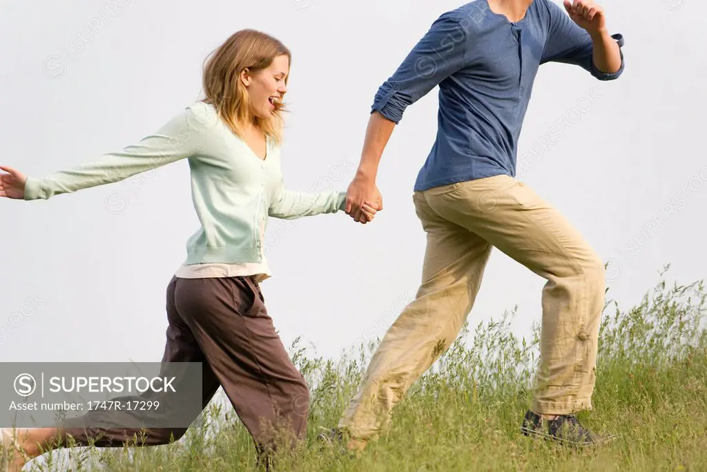 Young woman running on meadow with boyfriend
