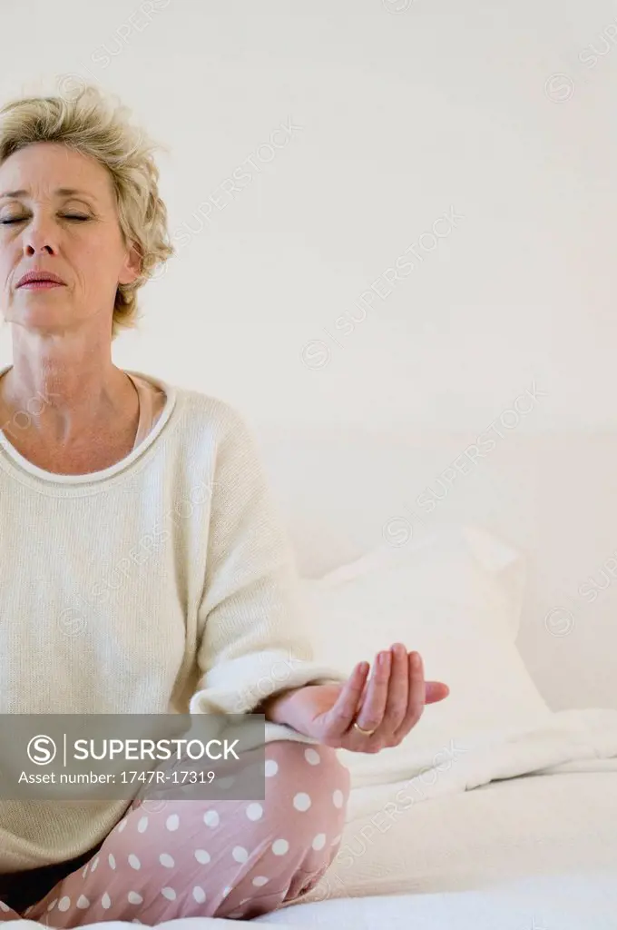 Mature woman meditating on bed, cropped
