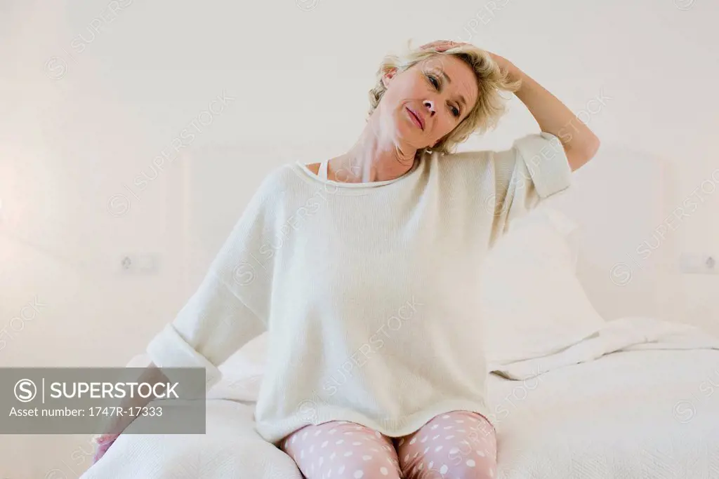 Mature woman kneeling on bed stretching neck
