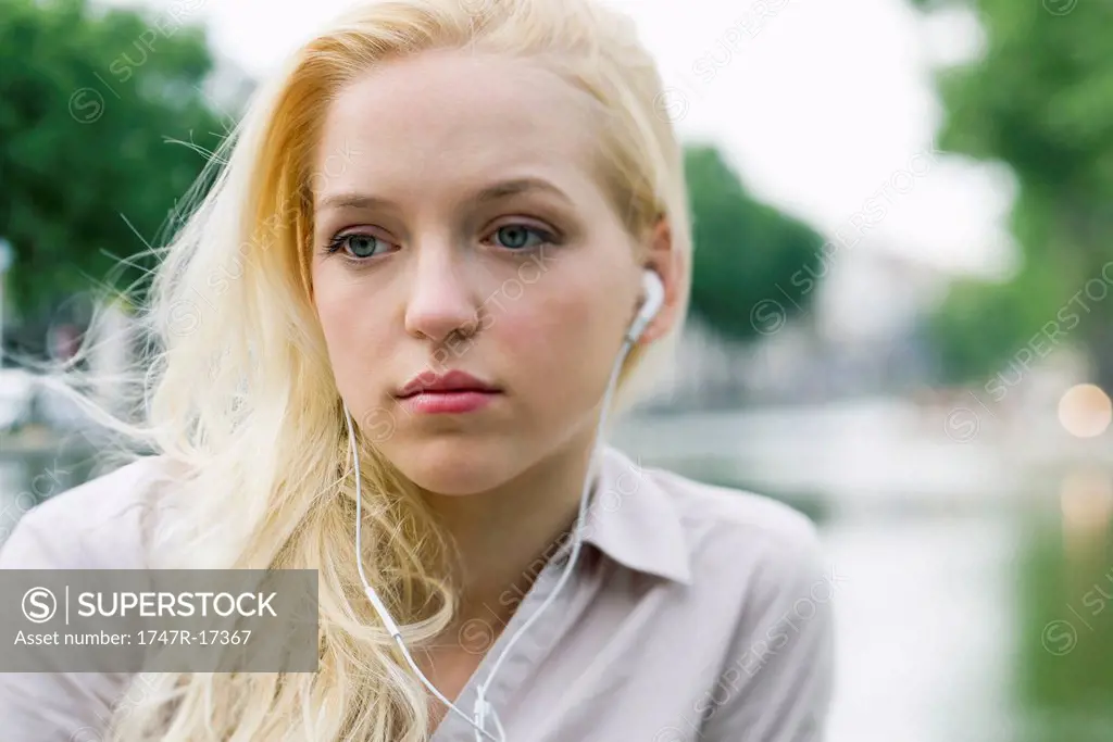 Young woman listening to earphones, looking away in thought