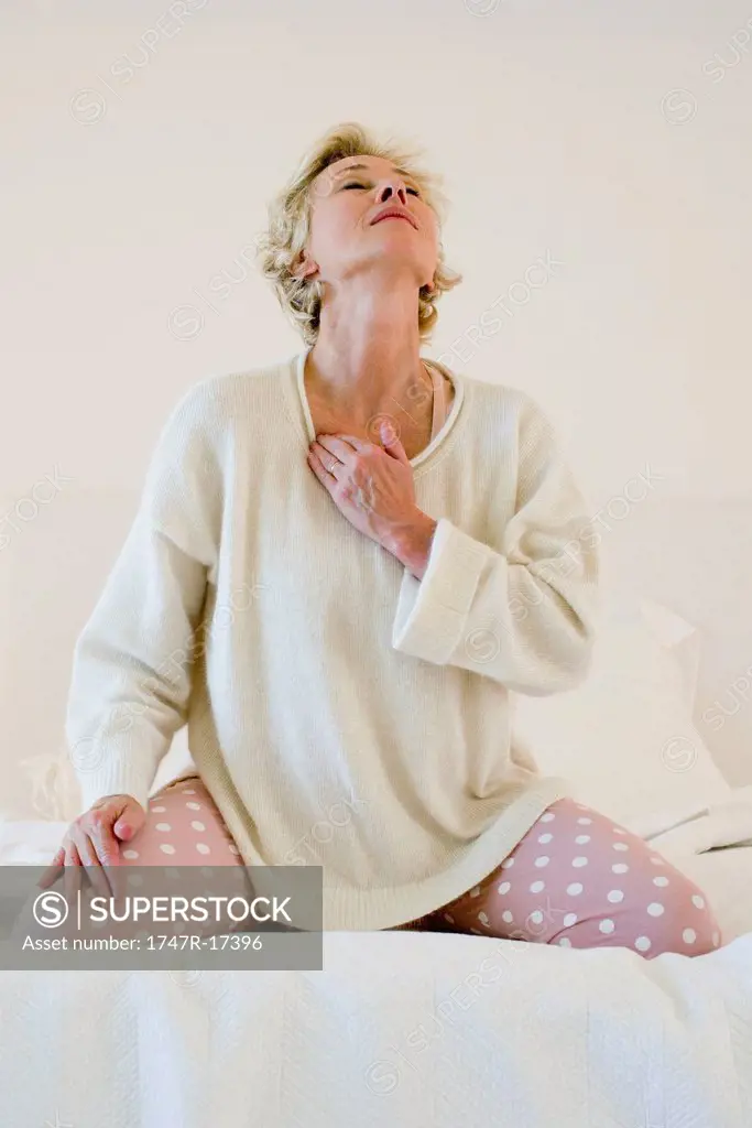 Mature woman kneeling on bed massaging neck