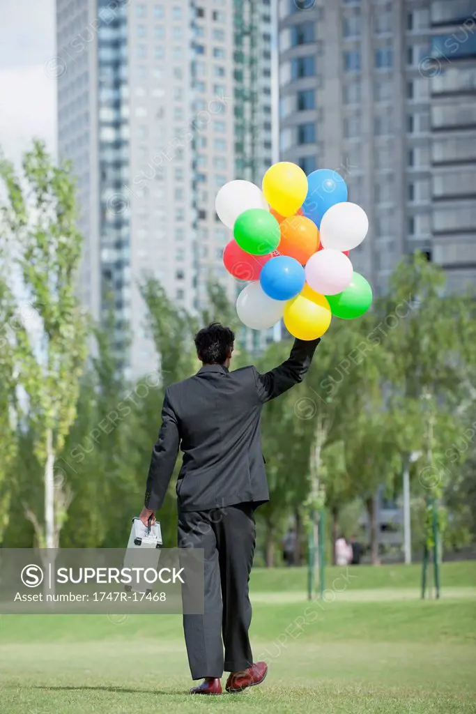 Businessman walking with bunch of balloons, rear view