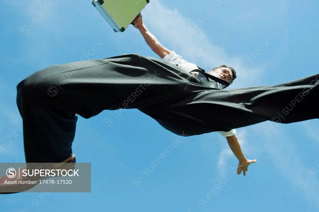 Businessman jumping in air carrying briefcase, directly below