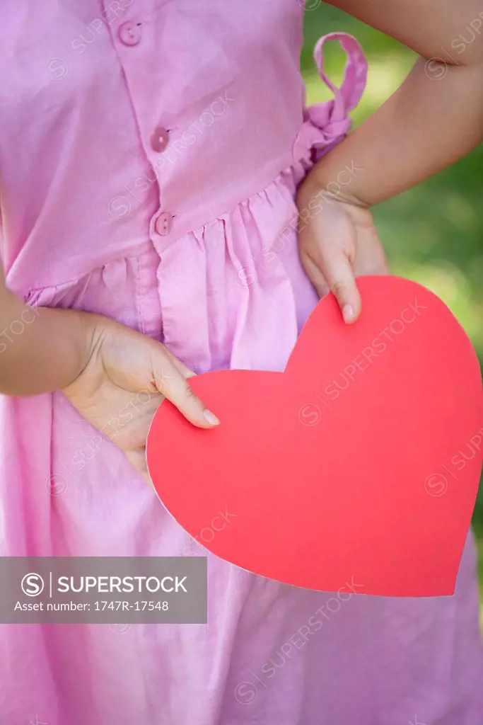 Girl holding paper heart behind back, cropped