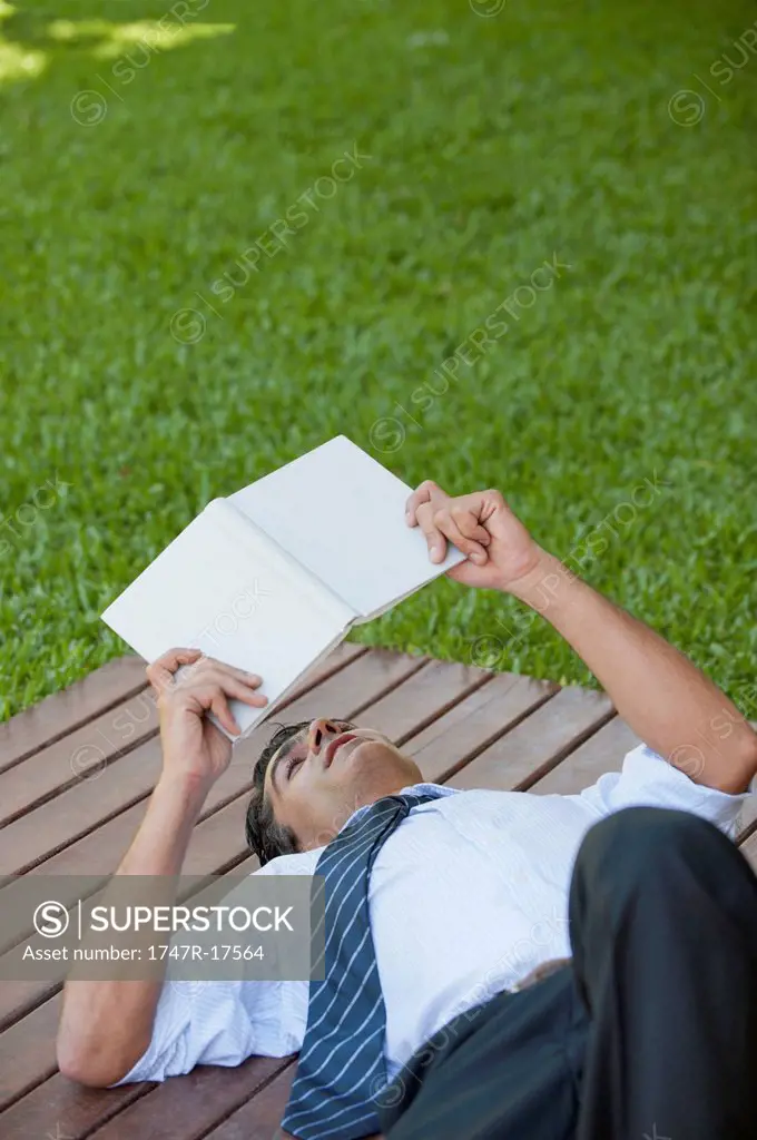 Man lying outdoors reading book