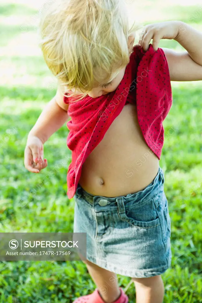 Baby girl lifting shirt up, looking curiosly at abdomen
