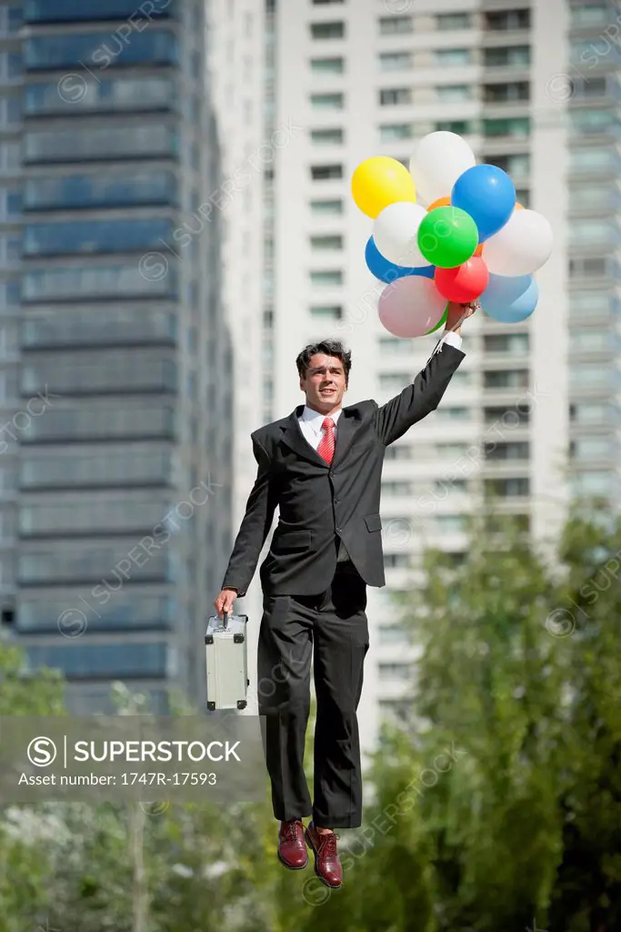 Businessman being carried away by bunch of balloons