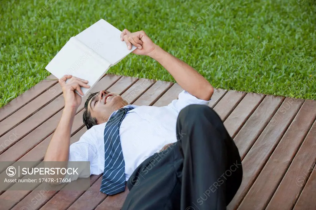 Mid_adult man lying outdoors reading book