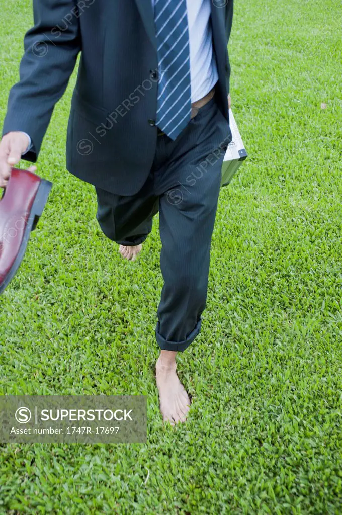 Businessman running barefoot on grass