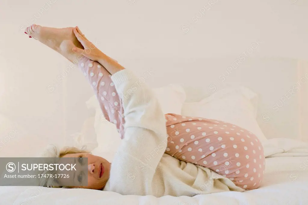 Mature woman lying on bed stretching legs